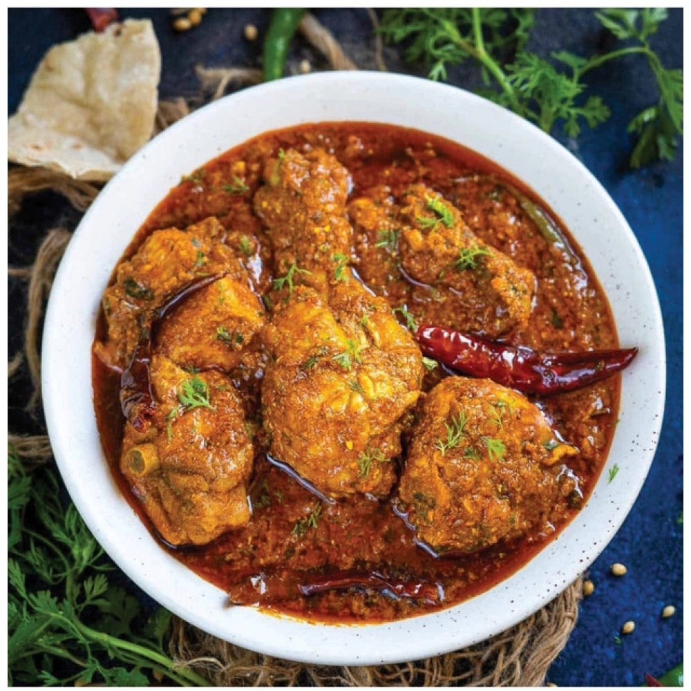 Chicken masala curry in a bowl with meat pieces, chili, and green herbs